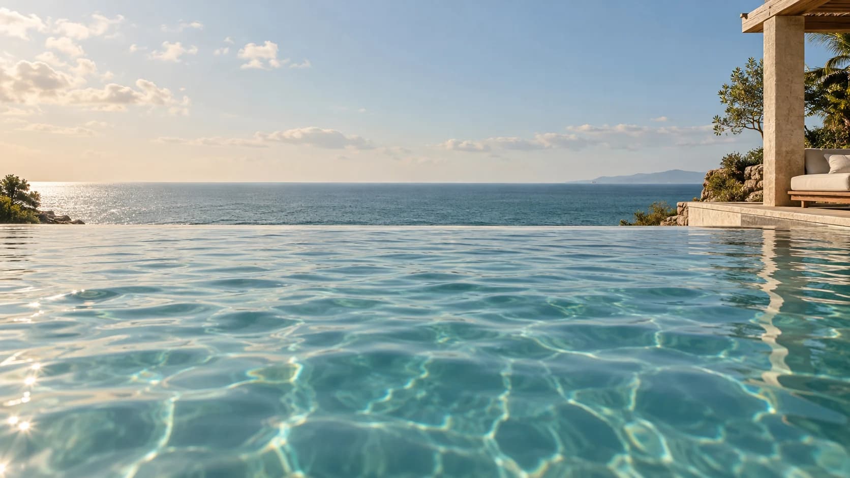 A low view across the infinity pool towards the open ocean and horizon, framed by warm limestone and teak